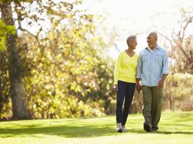 A senior couple smiling and holding hands while walking through a park