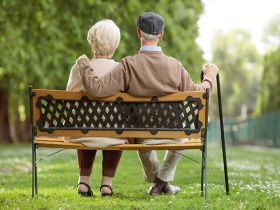 A view from behind of a senior couple sitting close together on a park bench